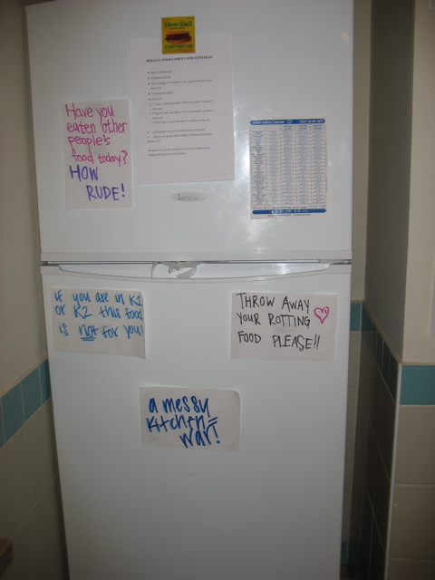 Four signs on the fridge: "Have you eaten other people's food today? How rude!" "If you are in K1 or K2 this food is not for you!" "Throw away your rotting food please!!" "A messy kitchen = war!"