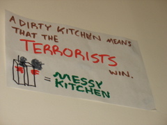 Sign posted very high in the kitchen: "A dirty kitchen means that the terrorists win. [Twin towers on fire] = Messy Kitchen"